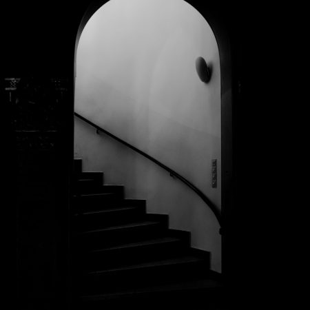 A high angle grayscale shot of an arch and a staircase surrounded by the dark background